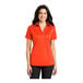 A woman wearing a Port Authority neon orange short sleeve polo shirt.