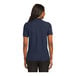 A woman wearing a navy Port Authority silk touch polo shirt.