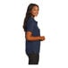 A woman wearing a navy Port Authority silk touch polo shirt.