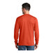 A man wearing an orange Port & Company long sleeve T-shirt.