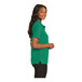 A woman wearing a Port Authority Kelly Green polo shirt.