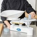 A man weighing something on an Edlund baker's dough scale on a table.