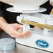 A person's hand using a white Edlund baker's dough scale to weigh a jar.