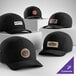 A collection of customizable black 7-panel brushed camper caps with various logo patches on the front.
