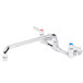 A chrome Advance Tabco wall-mount faucet with red knobs.