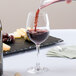 A person pouring red wine into a Stolzle Port/Sherry wine glass on a table in a winery cellar.