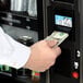 A hand inserting a dollar bill into a VEND MACH CD 10 SLT MECH & VAL vending machine.