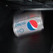 A close-up of a soda can falling into a white vending machine.