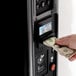 A hand inserting a dollar bill into a vending machine.