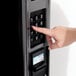 A finger pressing a number on a black keypad on a vending machine.