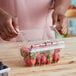 A woman holding a D&W Fine Pack plastic container of strawberries.