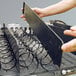 A person's hands holding a metal tray with black wires.