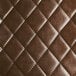 A close up of a brown tufted vinyl seat on a black chair.