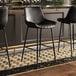 Three Lancaster Table & Seating black bar stools with black tufted vinyl seats at a bar.
