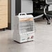 A portable white electric radiant and forced air heater with a protective metal grill and control knobs, placed on an office floor.