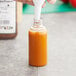 A person's hand pouring orange liquid from a white spoon into a 2 oz. PET Boston round bottle.