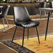 A Lancaster Table & Seating black chair with black tufted vinyl seat sits in front of a table in a restaurant dining area.