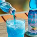 A blue bottle of Hana Ramune Blue Hawaii soda being poured into a glass of blue liquid.