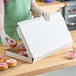 A woman in a green apron putting pink donuts into a white bakery box.