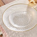 A clear plastic Visions coupe plate with a gold rim on a white tablecloth.