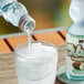 A Hana Ramune Coconut Soda bottle pouring liquid into a clear glass of ice.