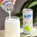 A hand pouring Milkis Apple Milk Soda into a glass with a straw.