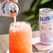 A hand pouring Milkis strawberry milk soda from a can into a glass.