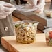 A person in gloves holding a Good Natured clear plastic deli container of pasta and olives.