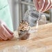 A gloved hand placing a cupcake with frosting and sprinkles in a clear plastic container.