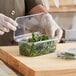 A hand in gloves cutting parsley into a clear plastic Good Natured herb container.