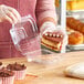 A woman in gloves holding a clear plastic container with a piece of cake inside.