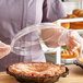 A woman in an apron holding a Good Natured clear plastic lid over a pie in a clear plastic container.