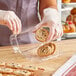 A woman in gloves putting cookies in a Good Natured clear plastic container.