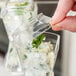 A hand placing a clear plastic lid over a small plastic cup filled with food.