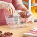 A woman in gloves placing a cupcake into a clear plastic Good Natured container.