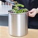 A person using a Vollrath stainless steel bain marie pot to serve green and red salad.