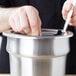 A person's hands using a spoon to stir a silver Vollrath inset.