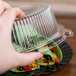 A hand holding a Fineline clear plastic lid over a food container.