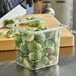 A clear plastic food pan with brussels sprouts inside on a counter being cut up.