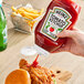 A hand pouring Heinz Ketchup from an upside-down bottle onto a chicken sandwich.