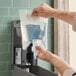 A hand using a Lavex bag of foaming hand sanitizer to refill a dispenser.