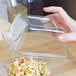 A hand holding a Fineline clear dome lid over pasta in a clear container.