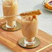Two glasses of brown liquid with a Fanale Golden Pear Rock Sugar syrup stick on a wooden table.