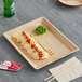 A rectangular Eco-gecko palm leaf tray with food on a wooden surface.