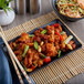 A black rectangular melamine tray with a plate of noodles, vegetables, and shrimp.