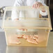 A chef holding a Carlisle yellow food storage box filled with raw chicken.