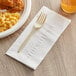 A plate of macaroni and cheese with fried chicken, a fork, and a Choice white square napkin with a black napkin band.