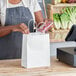 A woman in an apron holding a white Duro paper shopping bag with handles.