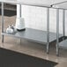 A Regency galvanized steel adjustable shelf for a work table under a metal work table with white containers on it.