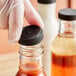 A hand wearing a white glove holding a plastic bottle with a black lid.